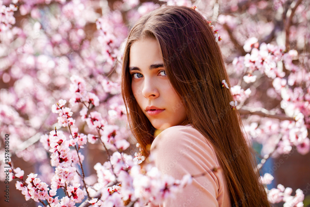 Fototapeta premium Young girl posing near blossom cherry tree with pink flowers