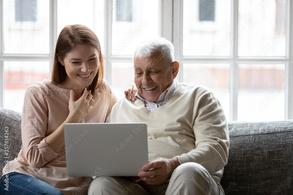 Happy older father and grownup daughter looking at laptop screen, having fun with computer, smiling mature man and young woman watching movie, shopping online, sitting on cozy couch at home Happy older father and grownup daughter looking at laptop screen, having fun with computer, smiling mature man and young woman watching movie, shopping online, sitting on cozy couch at home