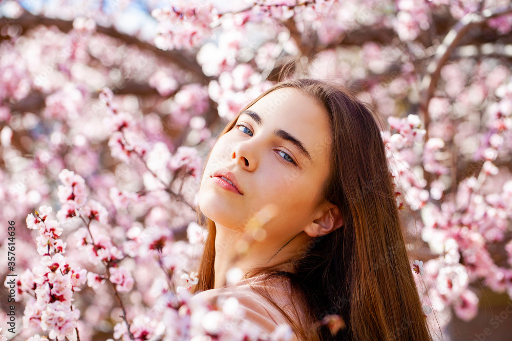 Young girl posing near blossom cherry tree with pink flowers