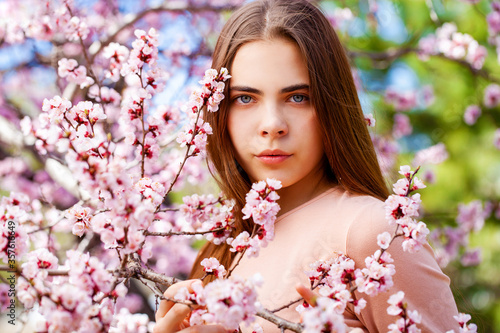 Young girl posing near blossom cherry tree with pink flowers