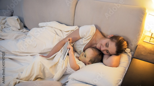 Cute little boy with young mother watching video on tablet before going to sleep