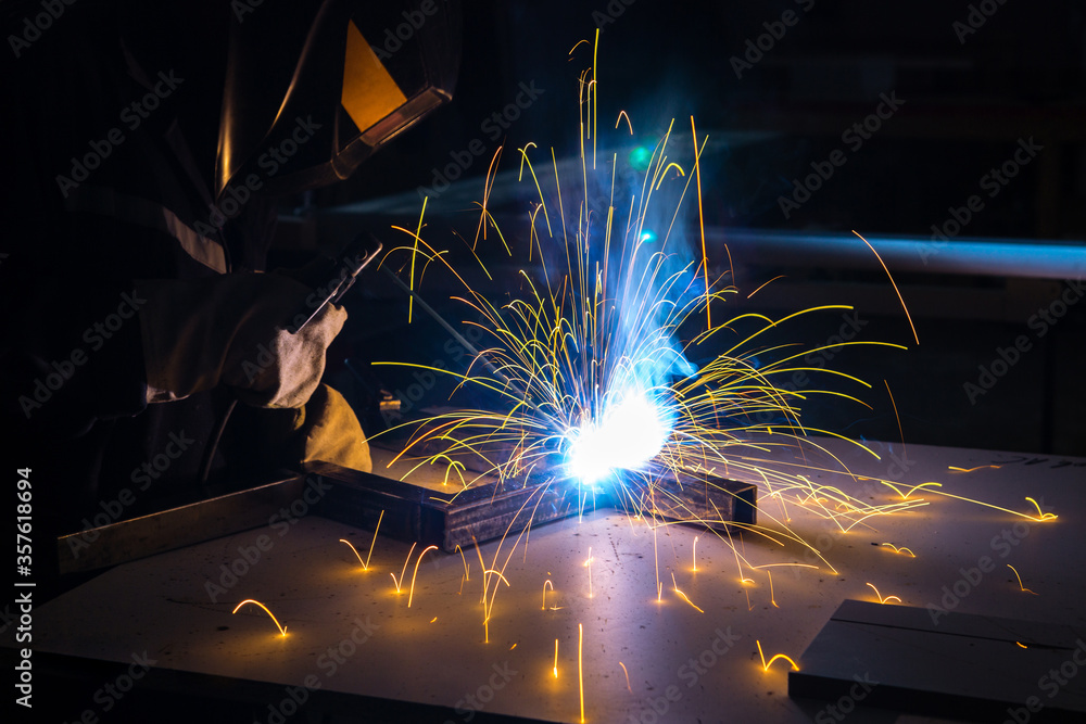 Metal welder working with arc welding machine to weld steel at factory while wearing safety equipment. Metal welder working with arc welding machine to weld steel at factory while wearing safety equipment.