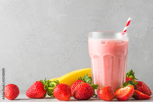 Strawberry and banana smoothie or milkshake in a glass with a straw with fresh fruits. refreshing summer drink