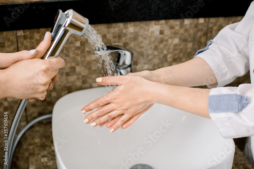 Close up of hands of female doctor cosmetologist, wearing white medical uniform, washing and rinsing off their hands in the sink with the help of her assistant, in modern spa beauty center