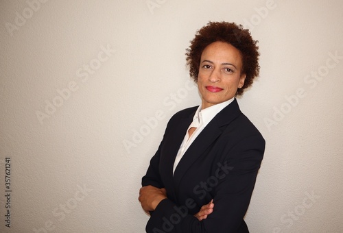 Bild auf Leinwand Successful, confident attractive black business woman wearing a dark suit standing with her arms folded and smiling positively