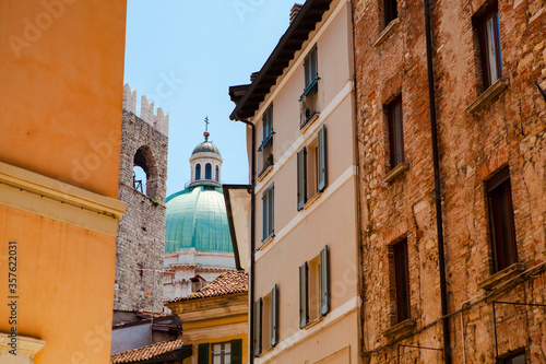 Close up. The view of the azure dome of the central cathedral (duomo) through vintage Italian buildings with shutters, balconies, tiled roofs in the historical centre of Brescia, Lombardy, Italy. © Andrei_Molchan