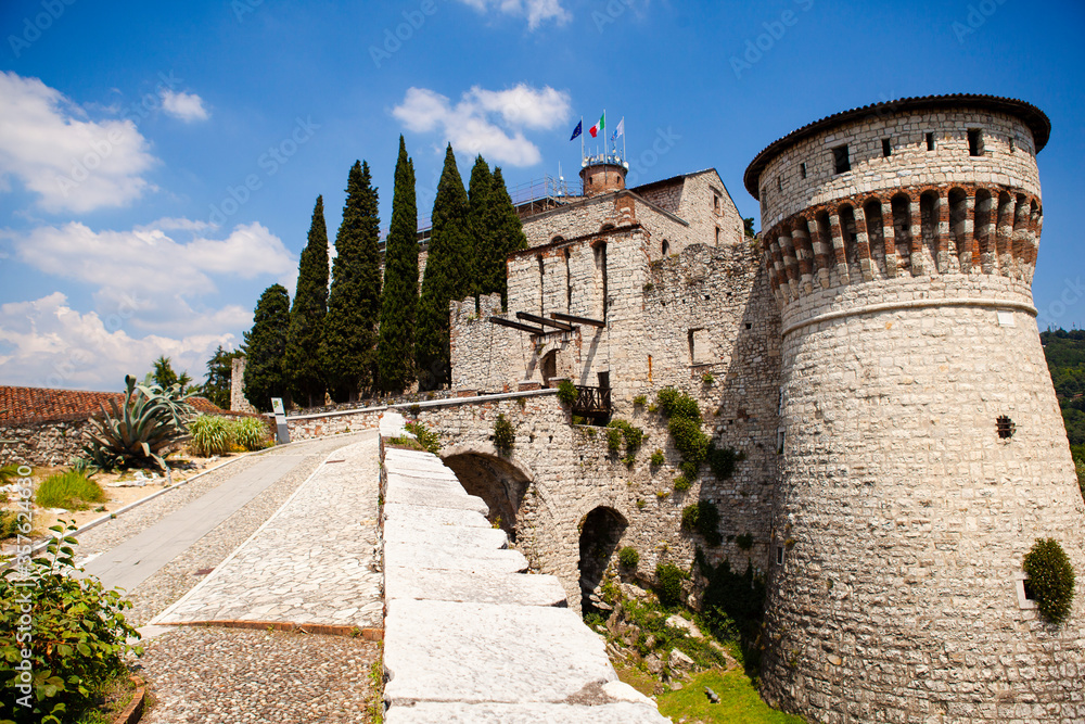 Obraz premium A medieval fortress (castle) with watchtowers, a trench and a walk-in bridge in front of the entrance made of white stones (bricks) in the center of the Italian city of Brescia (Lombardy, Italy).