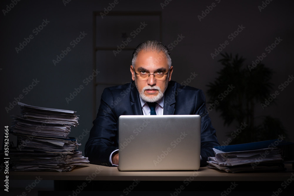 Old male employee working late at workplace Old male employee working late at workplace