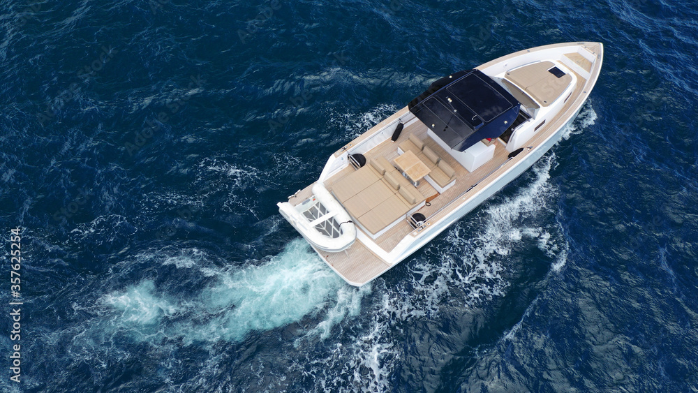 Aerial drone top down photo of small power boat with wooden deck cruising in deep blue Mediterranean sea Aerial drone top down photo of small power boat with wooden deck cruising in deep blue Mediterranean sea