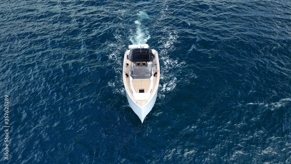 Aerial drone top down photo of small power boat with wooden deck cruising in deep blue Mediterranean sea