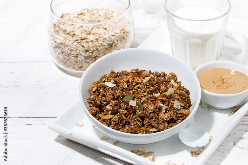 homemade chocolate granola, peanut butter and milk on white table homemade chocolate granola, peanut butter and milk on white table