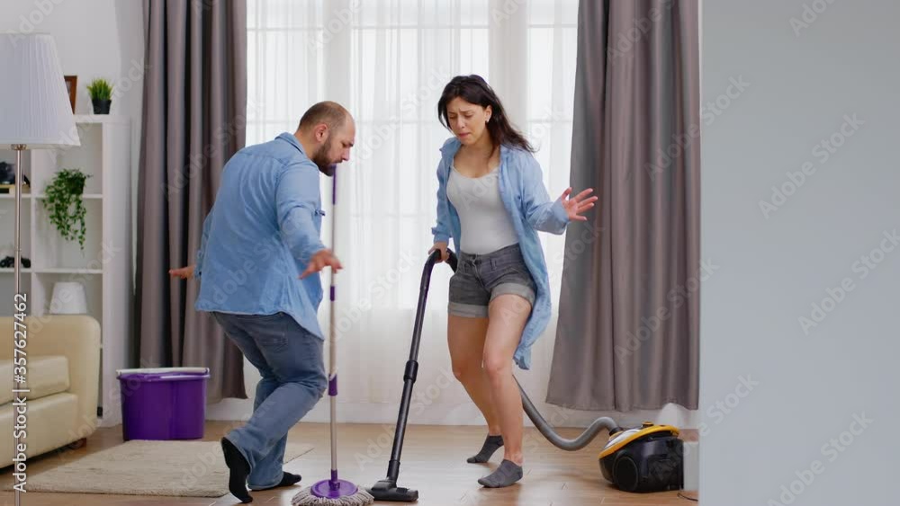 Happy dancing man and woman using vacuum and mop while cleaning the house. Happy dancing singing couple cleaning apartment, household and housekeeping, vaccum and mop, clean-up the house Happy dancing man and woman using vacuum and mop while cleaning the house. Happy dancing singing couple cleaning apartment, household and housekeeping, vaccum and mop, clean-up the house
