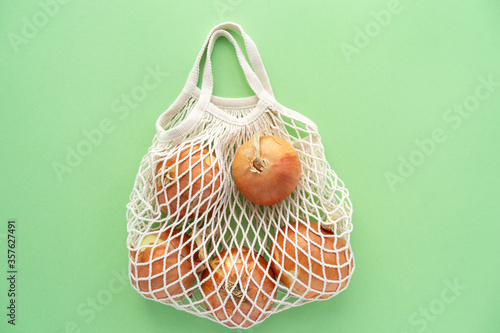 Grocery eco mesh cotton bag with onion.Vegetarianism. Eco friendly shopping and healthy lifestyle concept. Top view. Minimalism style. Flat lay onions on green background. Zero waste, plastic free