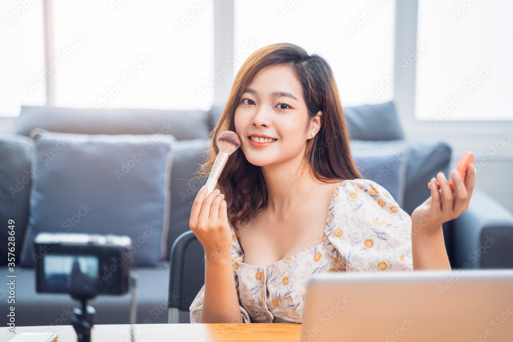 Asian beautiful businesswoman work from home live video camera recording interaction makeup tutorial using computer laptop vlogging selling products, internet social media influencer in living room Asian beautiful businesswoman work from home live video camera recording interaction makeup tutorial using computer laptop vlogging selling products, internet social media influencer in living room