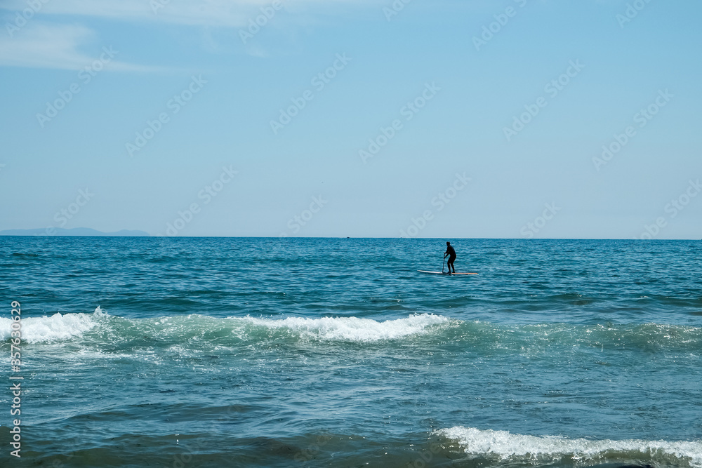 The man on the SUP board is floating in the bay in blue sea at sunny day. Active recreation in nature. A man spends a day enjoying SUP ride on the sea. Active lifestyle