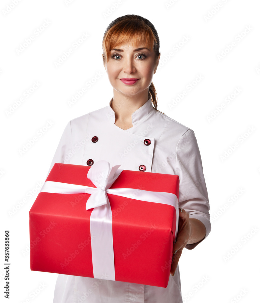 Portrait of young beautiful red-haired woman doctor or nurse in white special uniform standing holding big present box with ribbon Portrait of young beautiful red-haired woman doctor or nurse in white special uniform standing holding big present box with ribbon