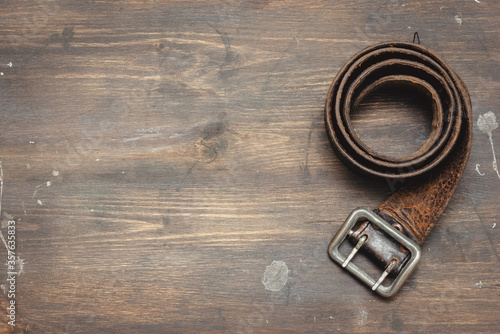 Old leather belt on aged wooden table background with copy space.