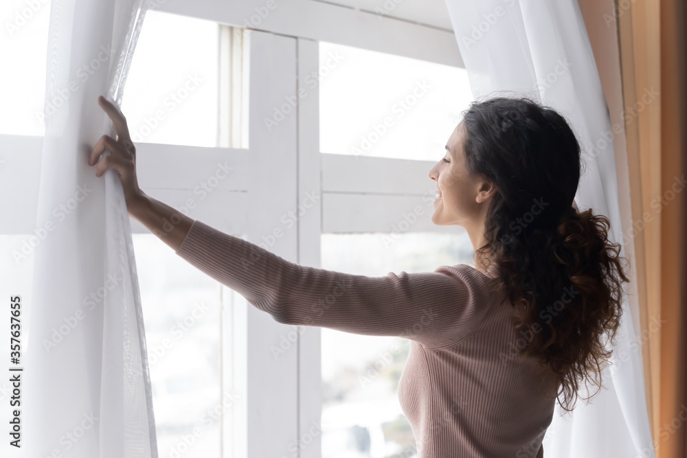Close up smiling woman opening curtains in morning, enjoying sunlight, standing at home, happy overjoyed young female looking out window, dreaming, starting new day, planning good future Close up smiling woman opening curtains in morning, enjoying sunlight, standing at home, happy overjoyed young female looking out window, dreaming, starting new day, planning good future