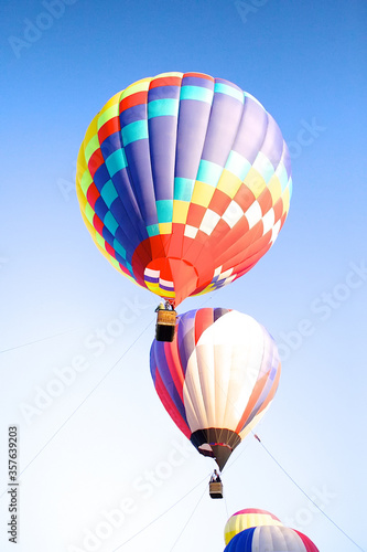 View of bright colored balloons balloons in flight on a beautiful Sunny day blue sky. The balloon fest is a vertical photo. People sit in baskets of balloons.