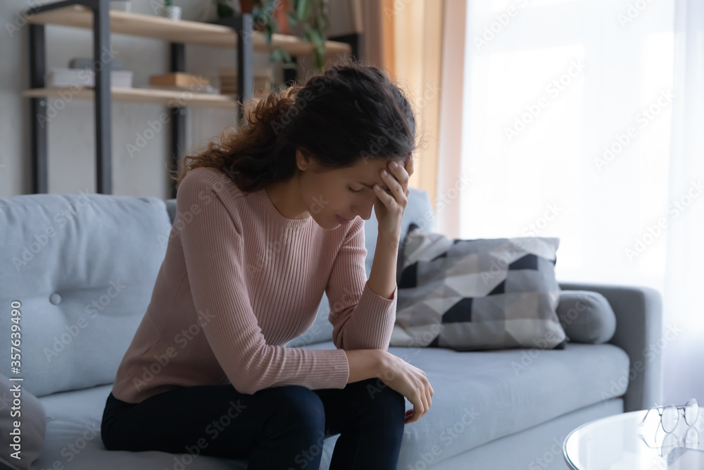 Unhappy stressed woman touching forehead, sitting on couch alone, thinking about personal life problems, break up or divorce, unexpected pregnancy, frustrated young female suffering from headache Unhappy stressed woman touching forehead, sitting on couch alone, thinking about personal life problems, break up or divorce, unexpected pregnancy, frustrated young female suffering from headache