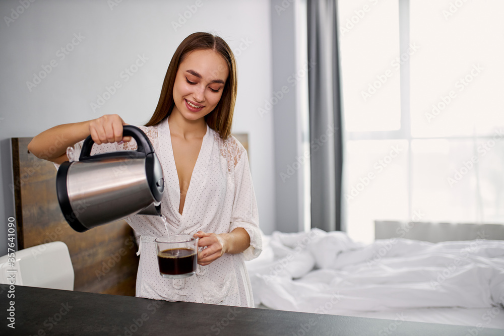 young good-looking caucasian female going to drink hot coffee at home, woman in bathrobe is pouring coffee into a cup