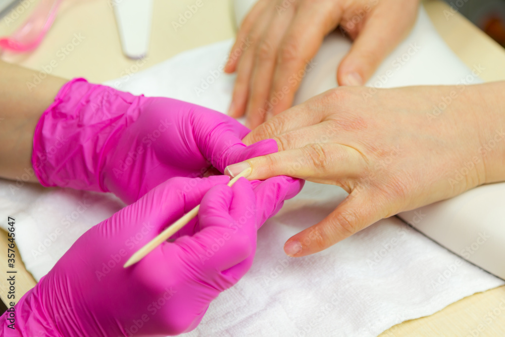 Fototapeta premium Nail care. Closeup of beautiful woman hands getting manicure in spa salon. Female manicurist cleaning cuticle with professional manicure pusher tool. Cosmetic procedure..