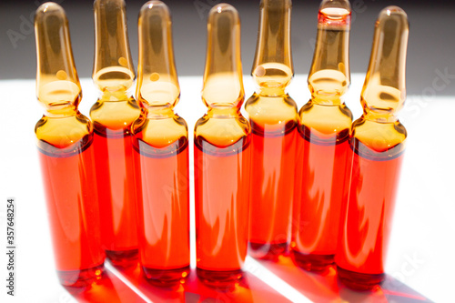 Seven red ampoules standing horizontally close-up on a white background backlit by sunlight. Vitamin B12.
