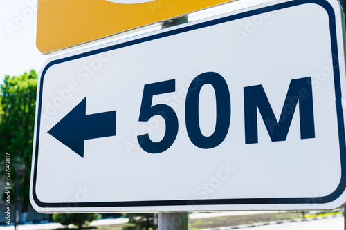 White rectangular road sign fifty meters with direction indicator. Metal sign pointer with an arrow 50 meters.