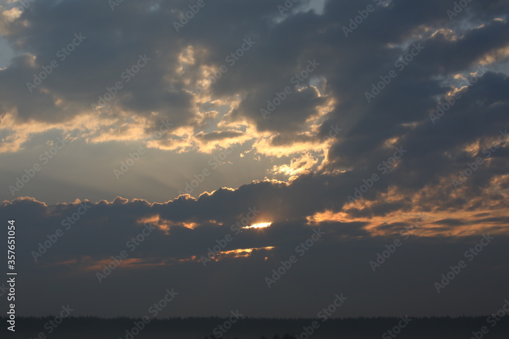 A cloudy landscape at dawn with grey clouds highlighted by the sun peeking out between them.Russia
