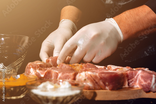 Marinating raw pork for cooking kebabs and ham. The chef of the restaurant in gloves treats the meat with basil and curry spices.