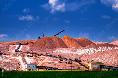 Industrial background. Salt mining site under blue bright sky. Large excavator machine and Huge mountains of waste ore in the extraction of potassium.