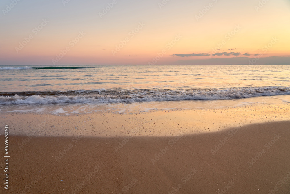Sandy beach on a sunset with reflection on wet sand and waves with foam. Copy space.