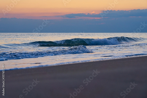 Sandy beach on a sunset with reflection on wet sand and waves with foam. Copy space.