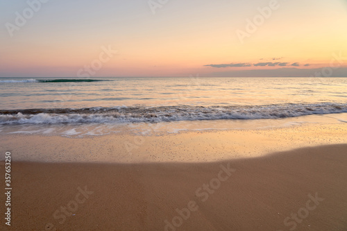 Sandy beach on a sunset with reflection on wet sand and waves with foam. Copy space.