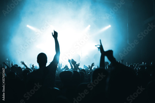 silhouette of a musical group on stage in the light of spotlights and the back of the crowd at a concert. music festival banner or poster in blue haze