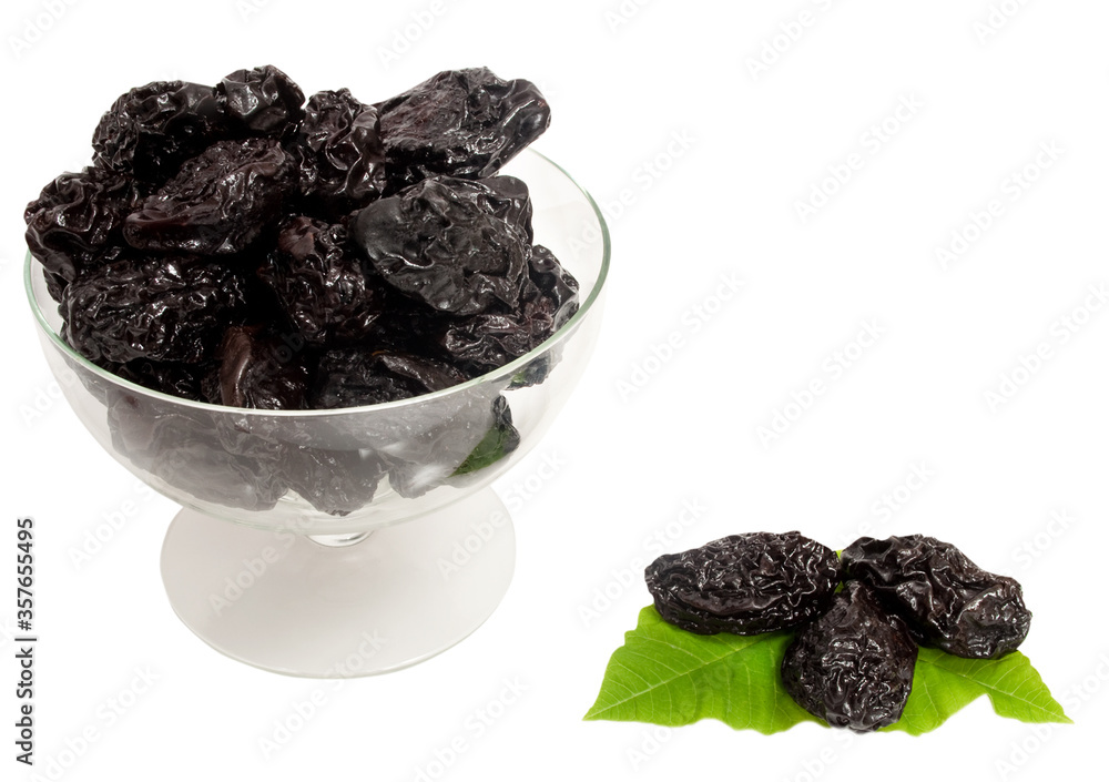 prunes in a glass bowl with green leaves isolated on white background prunes in a glass bowl with green leaves isolated on white background