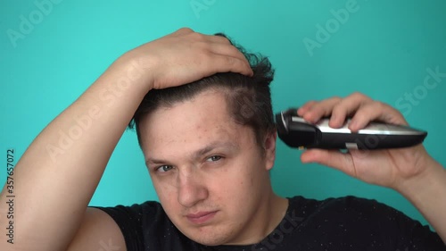 Brunette cuts himself with electric trimer. Smiles to himself. Blue background