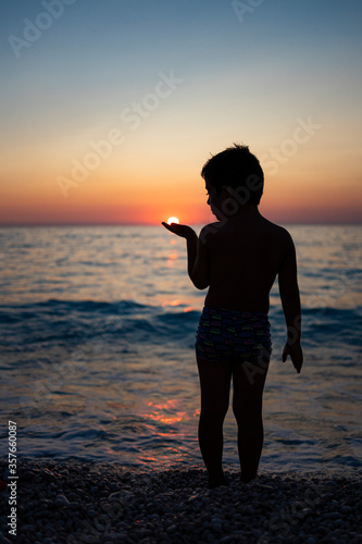 Little kid playing with the sun on the beach at sunset