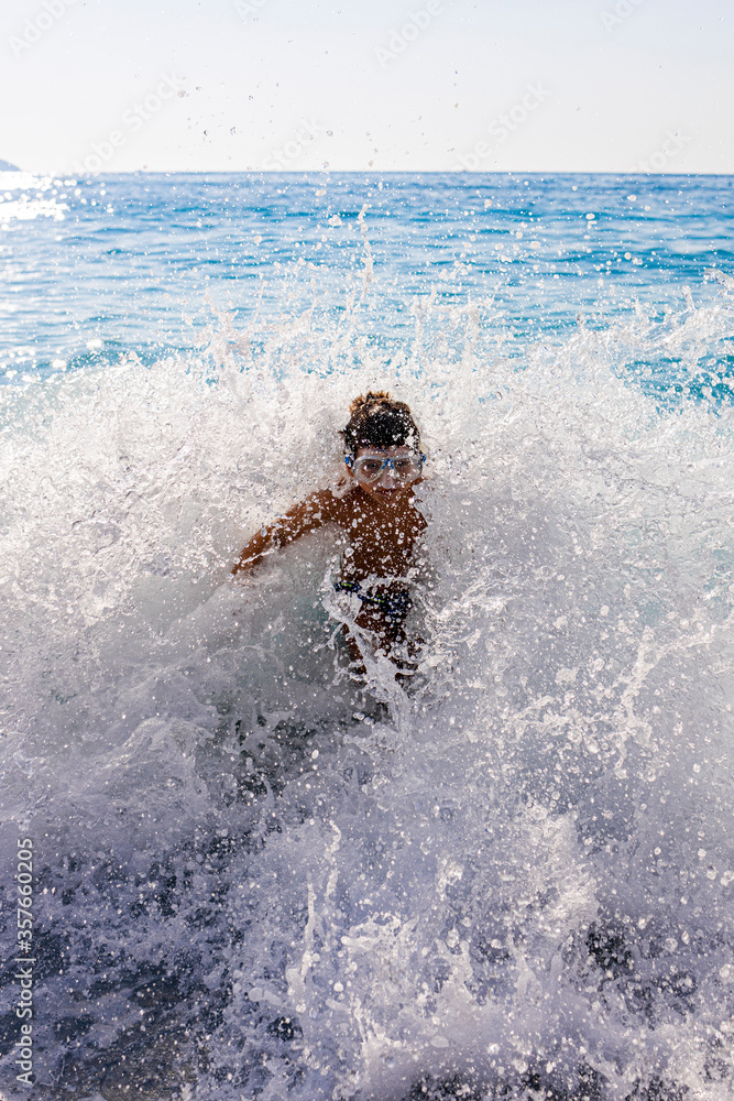 Little kid enjoying the waves on Myrtos beach, Greece.