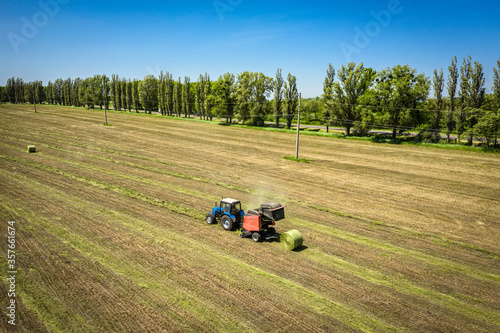 Small tractor with round baler unloading on a field