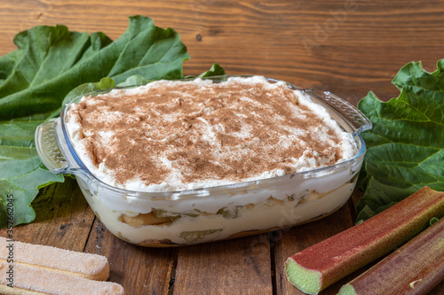 selbstgemachtes Tiramisu mit Rhabarber, Creme, Sahne, Zimt, Löffelbiscuit und Mascarpone auf einem Tisch aus Holz