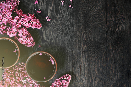 Background with two cups of tea on the dark wooden table and blooming lilac