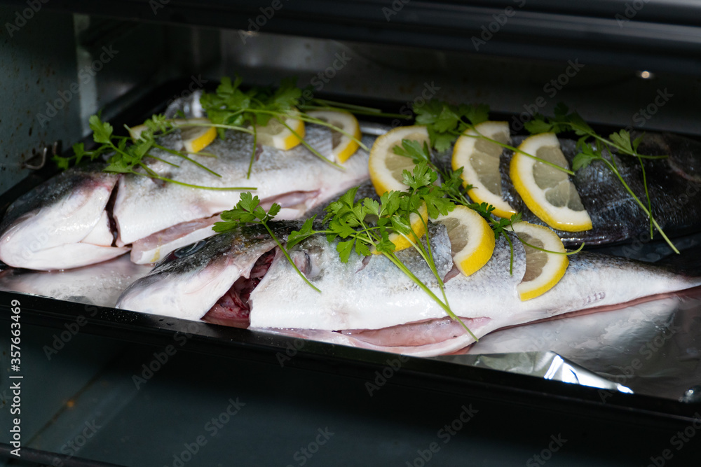 Fresh dorada fish with lemon and parsley on a baking sheet in the oven.