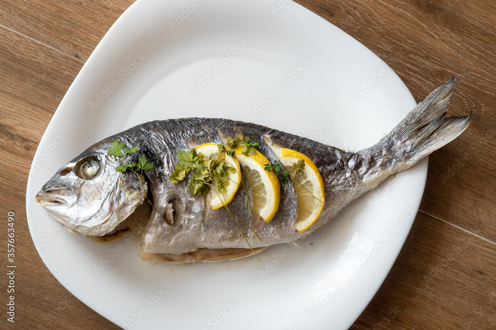 Dorada fish fried with lemon and parsley on a white plate. Fish fried