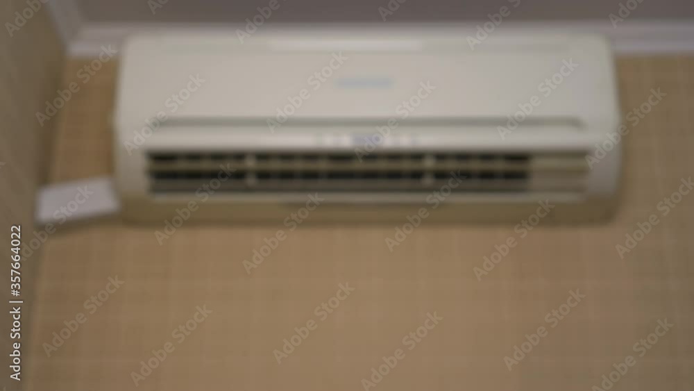 Air conditioning in the house to adjust the temperature in the room. A woman turns on the air conditioner using a remote control. Close-up. Air conditioner blurry Air conditioning in the house to adjust the temperature in the room. A woman turns on the air conditioner using a remote control. Close-up. Air conditioner blurry