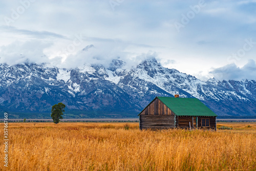 Grand Teton Range Peaks in the first snow and mist in autumn with a building of the T. A. Moulton barn inside Grand Teton National Park, Wyoming,United States of America (USA).