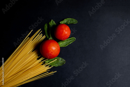 Spaghetti paste, tomato and other products for cooking on dark background top view. Space for text, top view