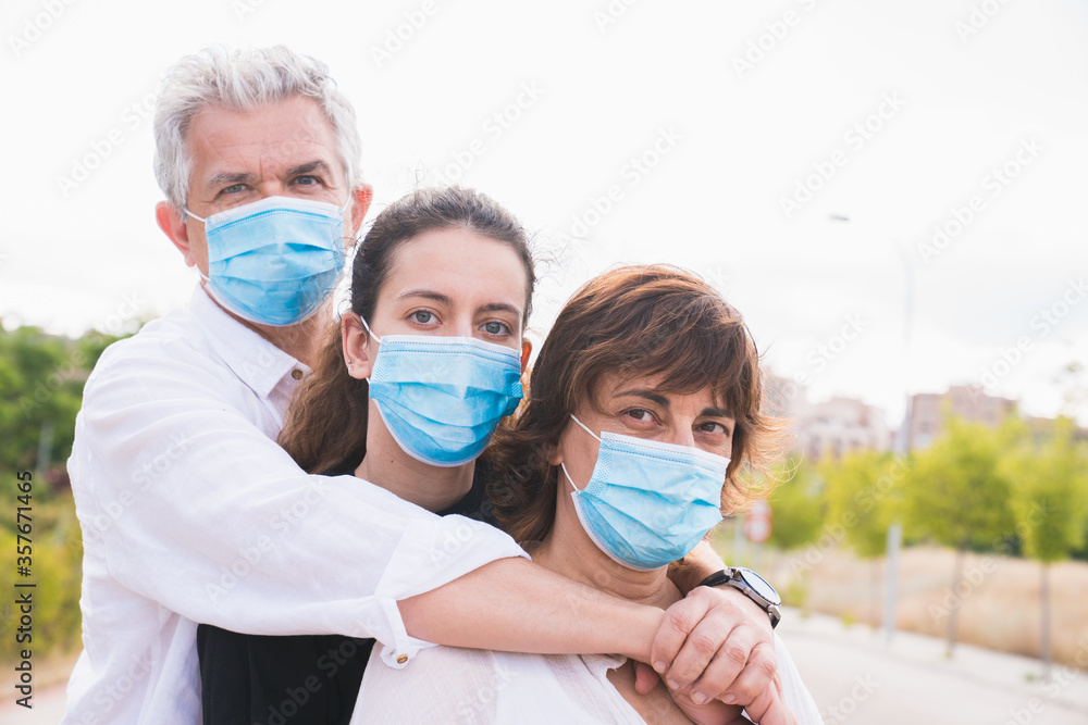 New normal. Masked family hugs. Members of a family hug each other with protective masks. Family protected with masks against coronavirus. Safety and pandemic concept. Coronavirus. Social distance.