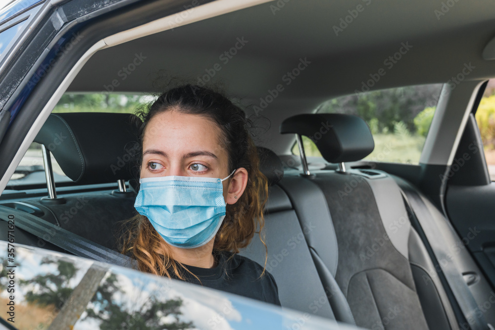 New normal. Teenager sitting in the back of a car with a mask. Young woman in a taxi protected by a mask. Safety and pandemic concept. Coronavirus devices. Social distance. New normal. Teenager sitting in the back of a car with a mask. Young woman in a taxi protected by a mask. Safety and pandemic concept. Coronavirus devices. Social distance.