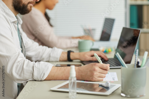 Side view portrait of unrecognizable bearded man reading document while working in office with colleagues in background, copy space